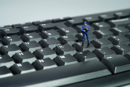 Miniaturmenschen Spielzeugfiguren Fotografie. Datenschutzkonzept. Ein Sicherheitsbeamter steht über der Tastatur. Vereinzelt auf weißem Hintergrund. Bild Foto