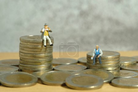 Miniaturmenschen Spielzeugfiguren Fotografie. Einkommens- und Vermögensschere, Ungleichheit. Zwei Menschen mit unterschiedlichen Jobs sitzen über einem Münzhaufen. Bild Foto