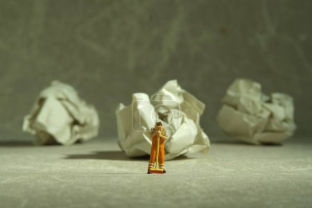 Miniature people toy figure photography. Tired sweeper standing in front of crumple ball of paper on the floor. Image photo