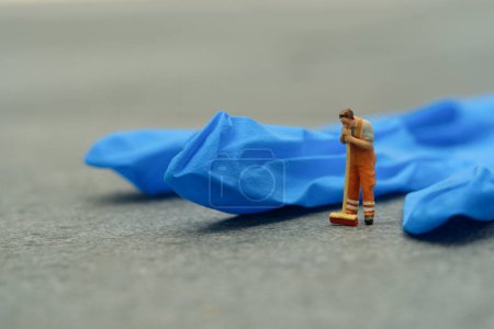 Photo for Miniature people toy figure photography. Tired sweeper cleaning worker standing in front of used blue latex glove. Image photo - Royalty Free Image
