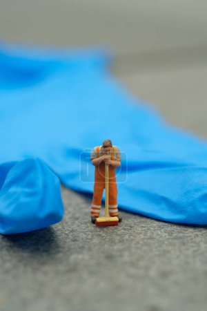 Photo for Miniature people toy figure photography. Tired sweeper cleaning worker standing in front of used blue latex glove. Image photo - Royalty Free Image