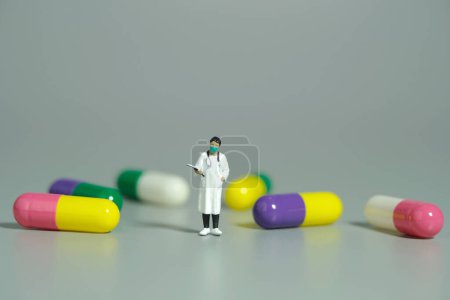 Photo for Miniature people toy figure photography. A female doctor standing in the middle of medicine pills. Isolated grey background. Image photo - Royalty Free Image