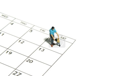 Miniature people toy figure photography. A father and son walking above calendar. Isolated white background. Image photo