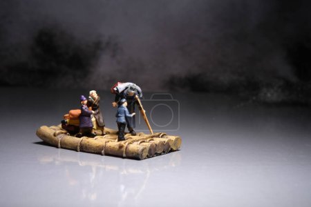 Téléchargez les photos : Miniature people toy figure photography. A group of poor family grandpa, grandma, and two grandchildren riding tree trunk raft at the night. Image photo - en image libre de droit