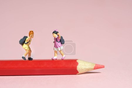 Foto de Miniatura gente pequeña juguetes fotografía. Dos niños parados encima del lápiz rojo. Aislado sobre fondo rosa. Foto de imagen - Imagen libre de derechos