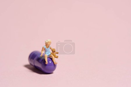 Photo for Miniature tiny people toy figure photography. A girl toddler sitting above purple medicine pill with teddy bear. Isolated on pink background. Image photo - Royalty Free Image