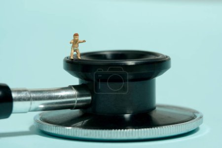 Foto de Miniatura gente pequeña juguete figura fotografía. Un niño pequeño caminando por encima del estetoscopio. Aislado sobre fondo azul. Foto de imagen - Imagen libre de derechos