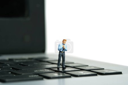 Photo for Miniature tiny people toy figure photography. A businessman getting ready, justify the tie standing above notebook keyboard. Isolated on white background. Image photo - Royalty Free Image