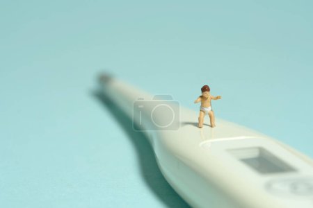 Foto de Miniatura gente pequeña juguete figura fotografía. Un niño pequeño bebé caminando por encima del termómetro sobre fondo azul. Foto de imagen - Imagen libre de derechos