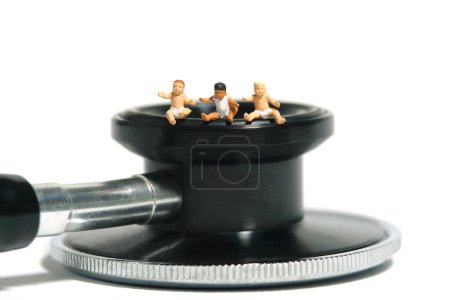 Foto de Miniatura gente pequeña juguete figura fotografía. Grupo de bebés pequeños sentados encima del estetoscopio. Aislado sobre fondo blanco. Foto de imagen - Imagen libre de derechos