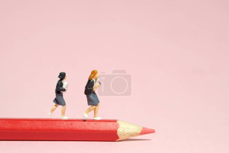 Foto de Miniatura gente pequeña juguetes fotografía. Dos estudiantes corriendo por encima del color rojo del lápiz. Aislado sobre fondo rosa. Foto de imagen - Imagen libre de derechos
