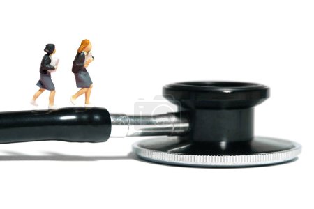 Miniaturmenschen Spielzeugfiguren Fotografie. Zwei Schülerinnen laufen über Stethoskop. Vereinzelt auf weißem Hintergrund. Bild Foto