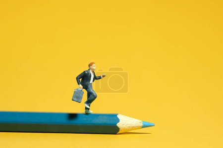 Foto de Miniatura gente pequeña juguetes fotografía. Un chico estudiante corriendo por encima del lápiz azul. Aislado sobre fondo amarillo. Foto de imagen - Imagen libre de derechos