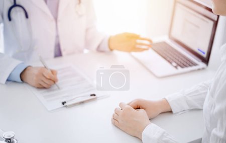 Foto de Médico y paciente usando tableta mientras están sentados uno frente al otro en el escritorio en la clínica. El foco está en las manos de las mujeres cerca del médico, de cerca. Concepto de medicina. - Imagen libre de derechos
