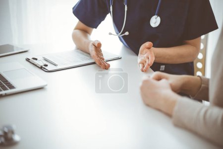 Foto de Médico y paciente sentados en la mesa en la clínica mientras discuten algo. El foco está en las manos de las médicas, de cerca. Concepto de medicina. - Imagen libre de derechos