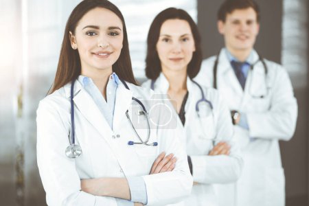 Photo for Group of young professional doctors standing as a team with arms crossed in sunny hospital. Medical help, insurance in health care, best disease treatment and medicine concept. - Royalty Free Image