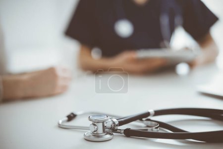 Foto de Estetoscopio acostado en la tableta frente a un médico y un paciente en el fondo. Medicina, concepto de salud. - Imagen libre de derechos