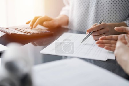 Woman accountant using a calculator and laptop computer while counting and discussing taxes with a client. Business audit and finance concepts.