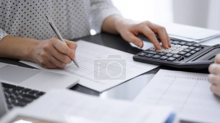 Woman accountant using a calculator and laptop computer while counting taxes with a client or a colleague. Business audit team, finance advisor.