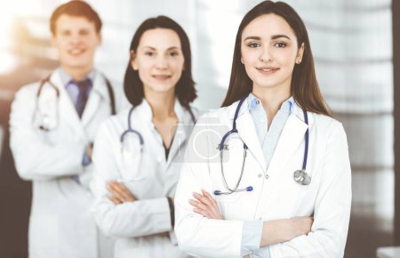 Group of young professional doctors standing as a team with arms crossed in sunny hospital. Medical help, insurance in health care, best disease treatment and medicine concept