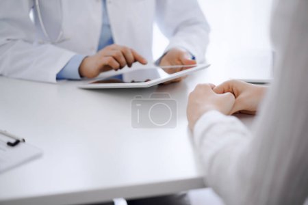 Foto de Doctor y paciente sentados uno frente al otro en el escritorio de la clínica. El enfoque está en las manos de los médicos femeninos usando tableta de computadora, de cerca. Concepto de medicina. - Imagen libre de derechos