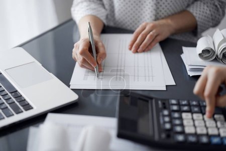 Femme comptable utilisant une calculatrice et un ordinateur portable tout en comptant les taxes pour un client. Audit d'entreprise et concepts financiers.