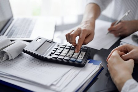 Woman accountant using a calculator and laptop computer while counting taxes for a client. Business audit and finance concepts.