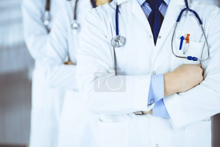 Photo for Group of modern doctors standing as a team with crossed arms and stethoscopes in hospital office. Physicians ready to examine and help patients. Medical help, insurance in health care - Royalty Free Image