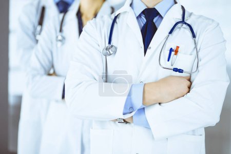 Photo for Group of modern doctors standing as a team with crossed arms and stethoscopes in hospital office. Physicians ready to examine and help patients. Medical help, insurance in health care - Royalty Free Image