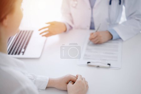Foto de Médico y paciente usando tableta mientras están sentados uno frente al otro en el escritorio en la clínica. El foco está en las manos de las mujeres cerca del médico, de cerca. Concepto de medicina. - Imagen libre de derechos