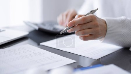 Woman accountant using a calculator and laptop computer while counting taxes for a client. Business audit concepts.
