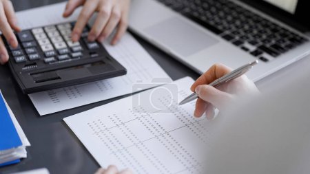 Woman accountant using a calculator and laptop computer while counting taxes for a client. Business audit concepts.