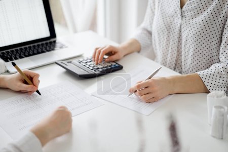 Two accountants using a calculator and laptop computer for counting taxes at white desk in office. Teamwork in business audit and finance.