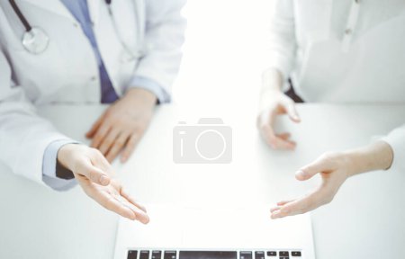 Foto de Doctor y paciente sentados uno al lado del otro en la mesa de la clínica. El enfoque está en las manos femeninas que apuntan a tableta táctil juntos. Concepto de medicina. - Imagen libre de derechos