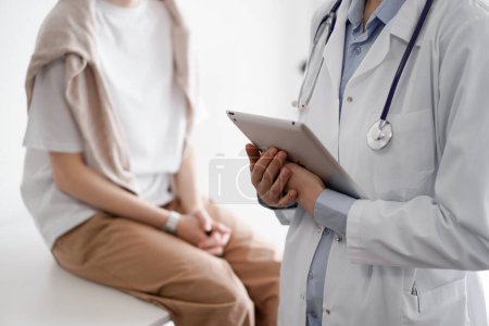 Arzt und Patient besprechen perfekte Untersuchungsergebnisse. Freundliche Ärztin hält Tablet-Computer mit den Händen in der Nähe einer jungen Frau. Medizinkonzept.
