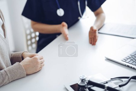 Foto de Médico y paciente sentados en la mesa en la clínica mientras discuten algo. El foco está en las manos de las pacientes femeninas, de cerca. Concepto de medicina. - Imagen libre de derechos