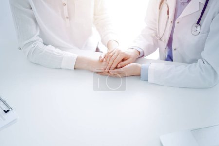 Photo for Doctor and patient sitting near each other at the table in clinic office. The focus is on female physicians hands reassuring woman, only hands, close up. Medicine concept. - Royalty Free Image
