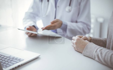 Foto de Médico y paciente sentado en la mesa de la clínica mientras usa la tableta. El foco está en las manos de las pacientes femeninas, de cerca. Concepto de medicina. - Imagen libre de derechos