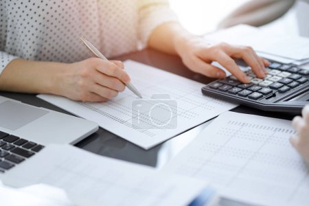 Woman accountant using a calculator and laptop computer while counting taxes with a client or a colleague. Business audit team, finance advisor.