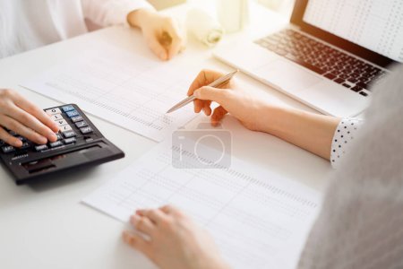 Two accountants using a laptop computer and calculator for counting taxes at white desk in office. Teamwork in business audit and finance.