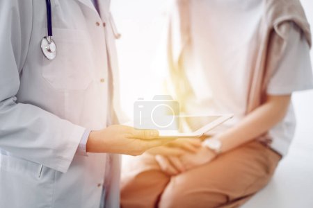 Doctor and patient discussing health exam results. Friendly physician reassuring a young woman by one hand while keeping tablet computer in another. Medicine concept.