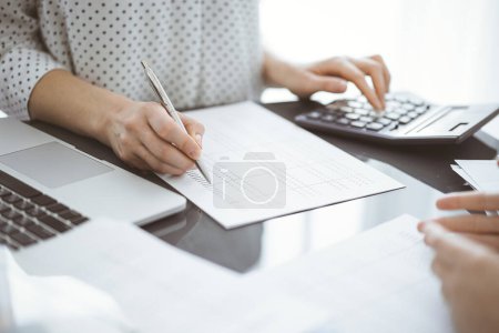 Woman accountant counting and discussing taxes with a client or a colleague while using a calculator and laptop computer. Business audit team.