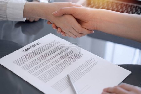 Photo for Business people shaking hands above contract papers just signed on the grey table, close up. Lawyers or entrepreneurs at meeting. Teamwork, partnership, success concept. - Royalty Free Image