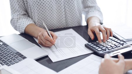 Foto de Mujer contable usando una calculadora y una computadora portátil mientras cuenta impuestos con un cliente o un colega. Equipo de auditoría empresarial, asesor financiero. - Imagen libre de derechos