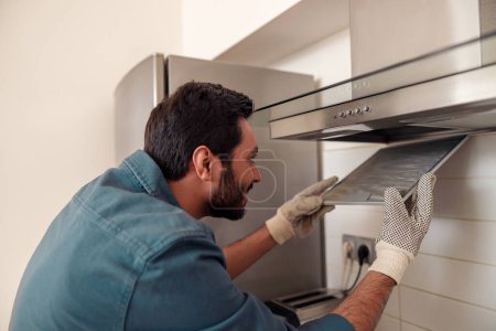 Téléchargez les photos : Service homme de réparation extracteur de cuisine, remplacement du filtre dans la hotte. Photo de haute qualité - en image libre de droit
