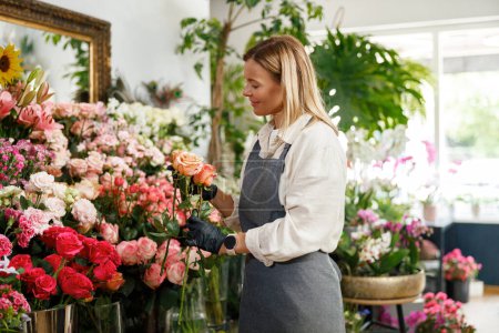 Téléchargez les photos : Fleuriste femme propriétaire de magasin de fleurs tenir des roses sur fond floral. Photo de haute qualité - en image libre de droit