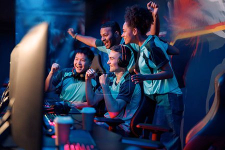 Multiracial Cyber-Sport-Spieler, die ihren Erfolg ausdrücken, während sie die Hände heben und lächeln während der Teilnahme am esports-Turnier im Computerclub
