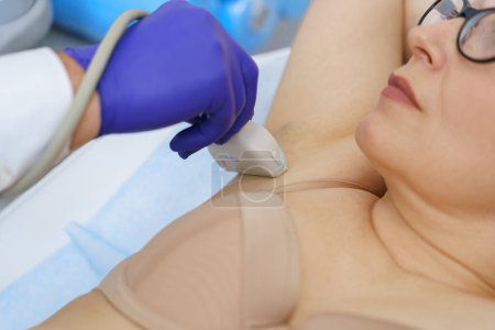 Téléchargez les photos : Gros plan de la femme a des ganglions lymphatiques ultrasonores dans la zone sous les aisselles de la clinique. Photo de haute qualité - en image libre de droit