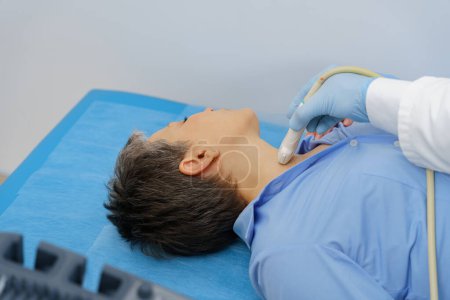 Téléchargez les photos : Patiente d'âge moyen lors d'un examen échographique de la thyroïde couchée sur le canapé dans un cabinet médical - en image libre de droit