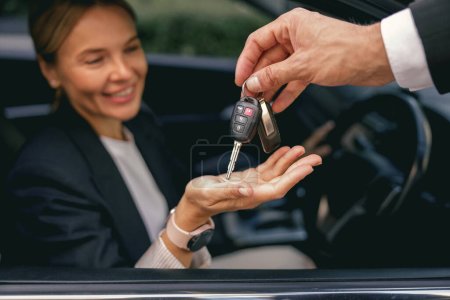 Großaufnahme einer lächelnden Geschäftsfrau im Anzug, die Autoschlüssel für ein neues Fahrzeug erhält